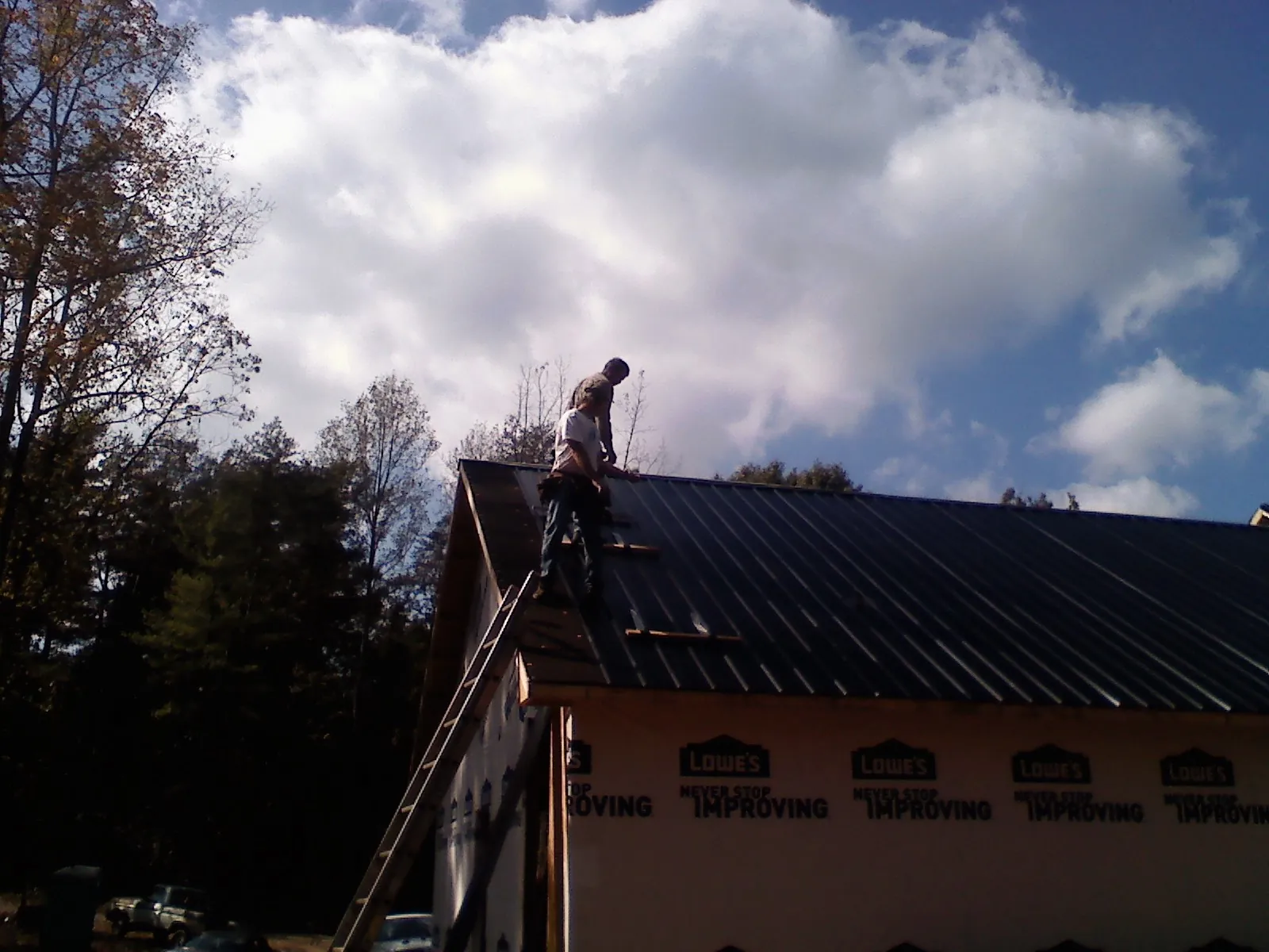 Roofer fastening dark metal panels high against a cloudy sky, from a Roof Inspection job in Haddonfield